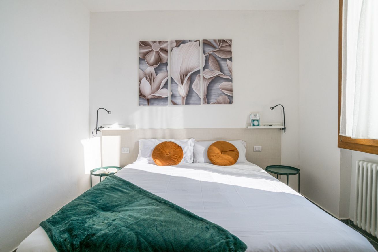 Un dormitorio con una cama, una manta verde, dos mesitas de noche, una repisa y una obra de arte en la pared.