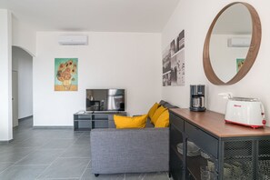 A modern living room with a grey sofa, yellow cushions, a flat-screen TV, a coffee maker, a toaster, and a large mirror. - GuestHost - Cosy and bright apartment of 65 sqm, located on the first floor of a building (without lift) with a shared garden and private parking space.The property is located in the lakeside village of Pusiano and enjoys a splendid lake view, which can  (Pusiano)
