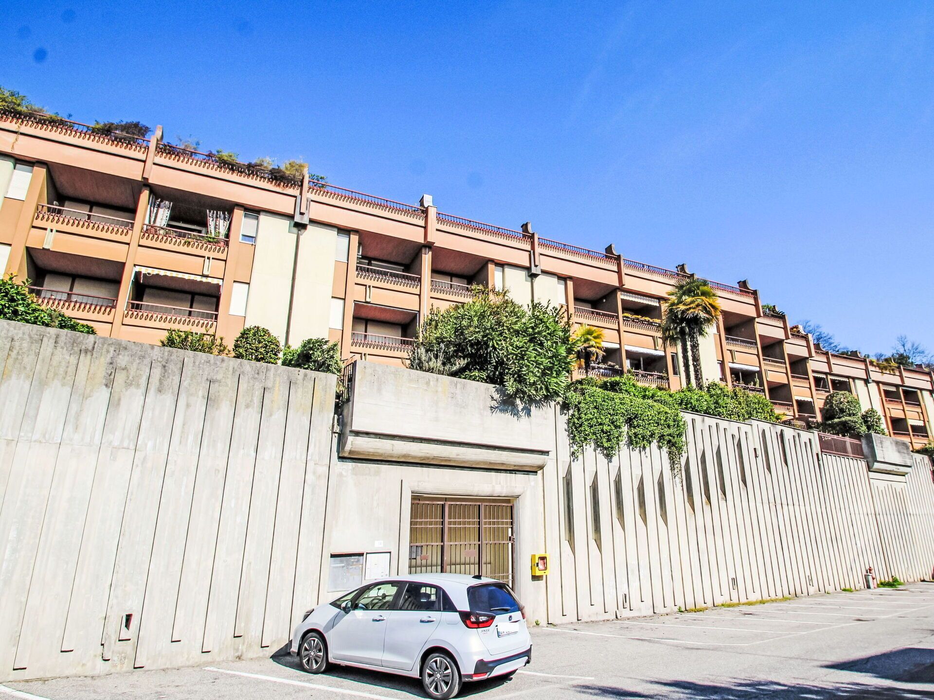 Un immeuble à plusieurs étages doté de balcons, d’une aire de stationnement et d’une voiture garée devant.