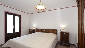 A bedroom with a large bed, two bedside tables with lamps, a wooden wardrobe, and a door with frosted glass panels.