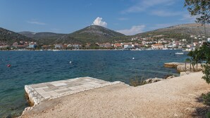 A coastal town with a clear view of the sea, a prominent hill, and a paved area in the foreground. - Perfect Beachfront Getaway Ideal for Families (Seget)