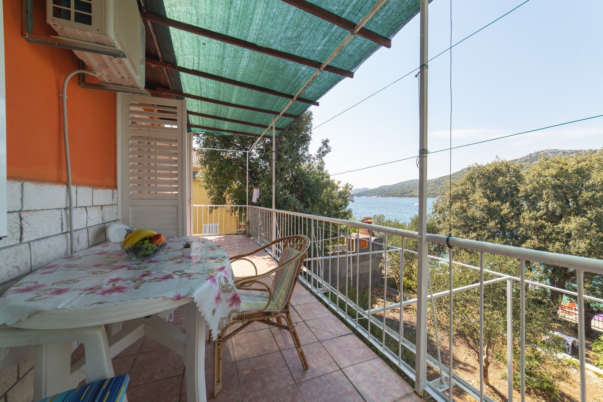 Ein Balkon mit Tisch und Stühlen, der einen schönen Blick auf einen See und Hügel bietet.