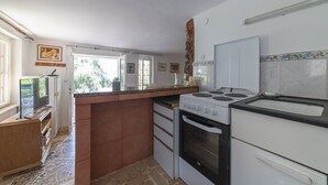 A kitchen with a stove, oven, and a sink. There is a window with a view of trees outside. - Perfect Beachfront Getaway Ideal for Families (Seget)