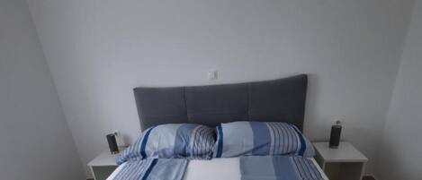 Een moderne slaapkamer met een bed, een grijs hoofdeinde en twee nachtkastjes met lampen.