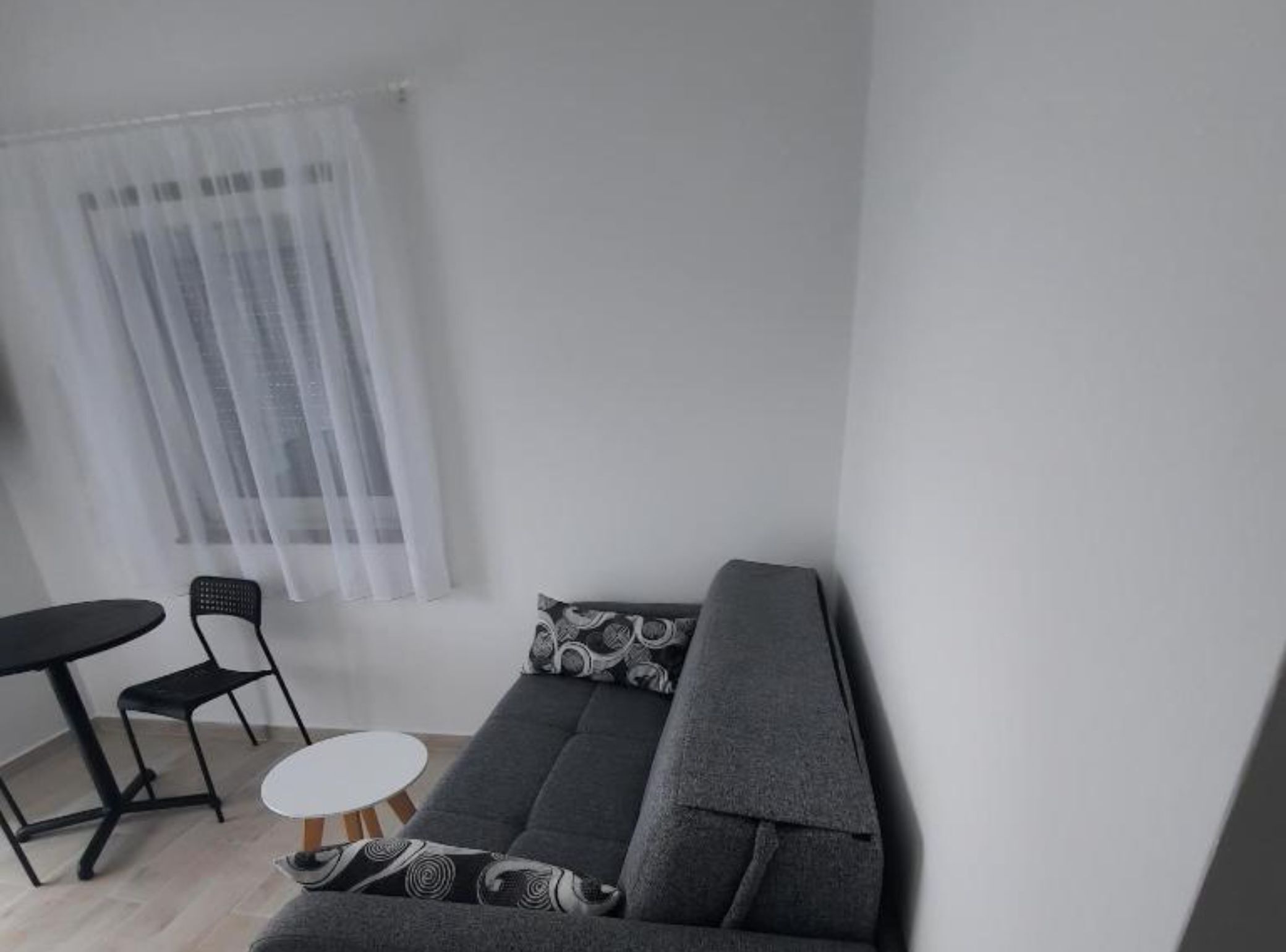 A modern living room with a grey sofa, a small round table, and two black chairs.