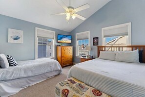 A bedroom with two beds, a ceiling fan, a TV, and a window with blinds.
