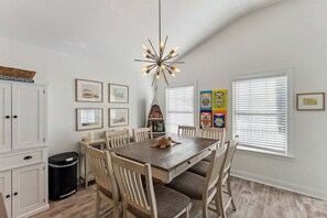 A dining area with a wooden table, white chairs, a unique ceiling light fixture, and framed artwork on the walls.
