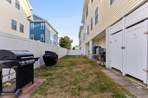 Un jardin à l’arrière d’une maison, équipé d’un barbecue, d’une poubelle et d’un espace barbecue couvert.