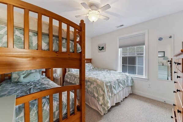 Une chambre avec un lit superposé, un lit simple, un ventilateur de plafond, une fenêtre avec des stores et un miroir.