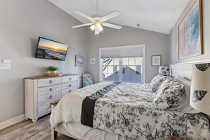 A bedroom with a bed, a dresser, a ceiling fan, a TV, and a window with blinds.