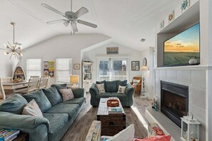 Ein geräumiges Wohnzimmer mit Kamin, Deckenventilator und großem, an der Wand befestigten Fernseher.