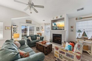 A living room with a fireplace, a ceiling fan, and a television mounted above it.