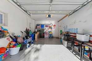 Eine Garage mit einem Bett, einem Tisch und verschiedenen Gegenständen wie einem Fahrrad, einer Waschmaschine und einem Eimer.