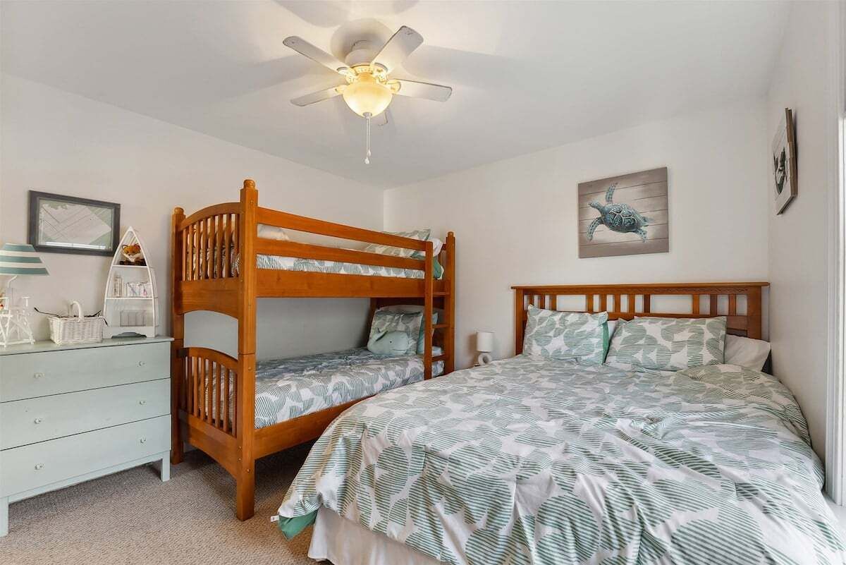A bedroom with a bunk bed, a single bed, a dresser, and a ceiling fan.