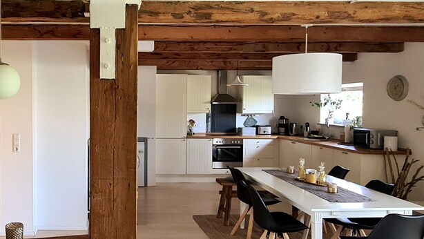 A modern kitchen with white cabinets, a wooden ceiling, and a dining area with a white table and black chairs. - Apartment 'Nordsee- Ferienwohnung Im Speicher' with Wi-Fi (Meldorf)