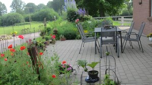 Un patio con mesa y sillas, rodeado de macetas con plantas y flores.