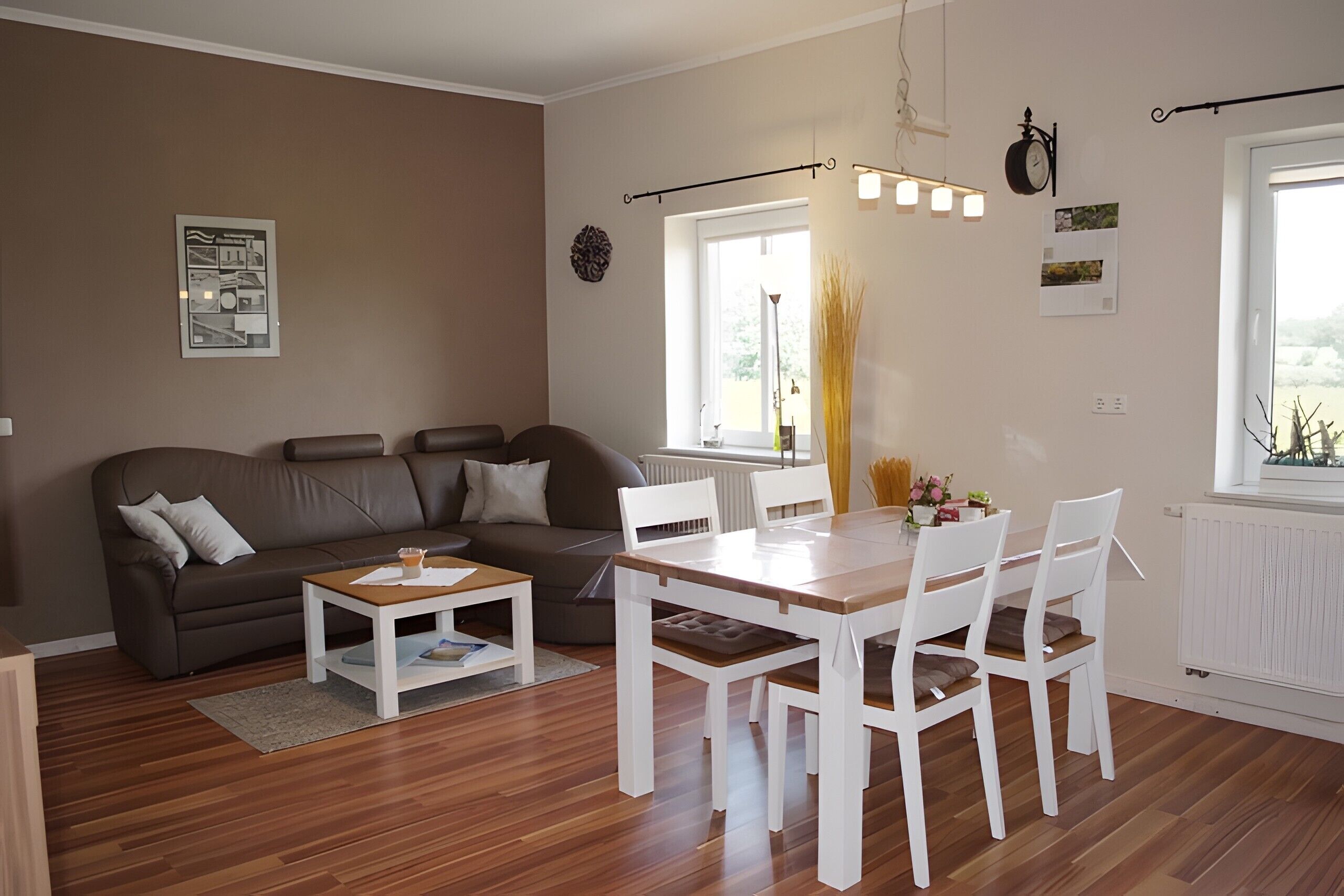 Ein modernes Wohnzimmer mit einer Couch, einem Couchtisch, einem Esstisch mit Stühlen, einem Fenster mit Vorhängen und einer Wanduhr.
