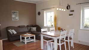 Una sala de estar moderna con un sofá, una mesa de centro, una mesa de comedor con sillas, un ventanal con cortinas y un reloj en la pared.