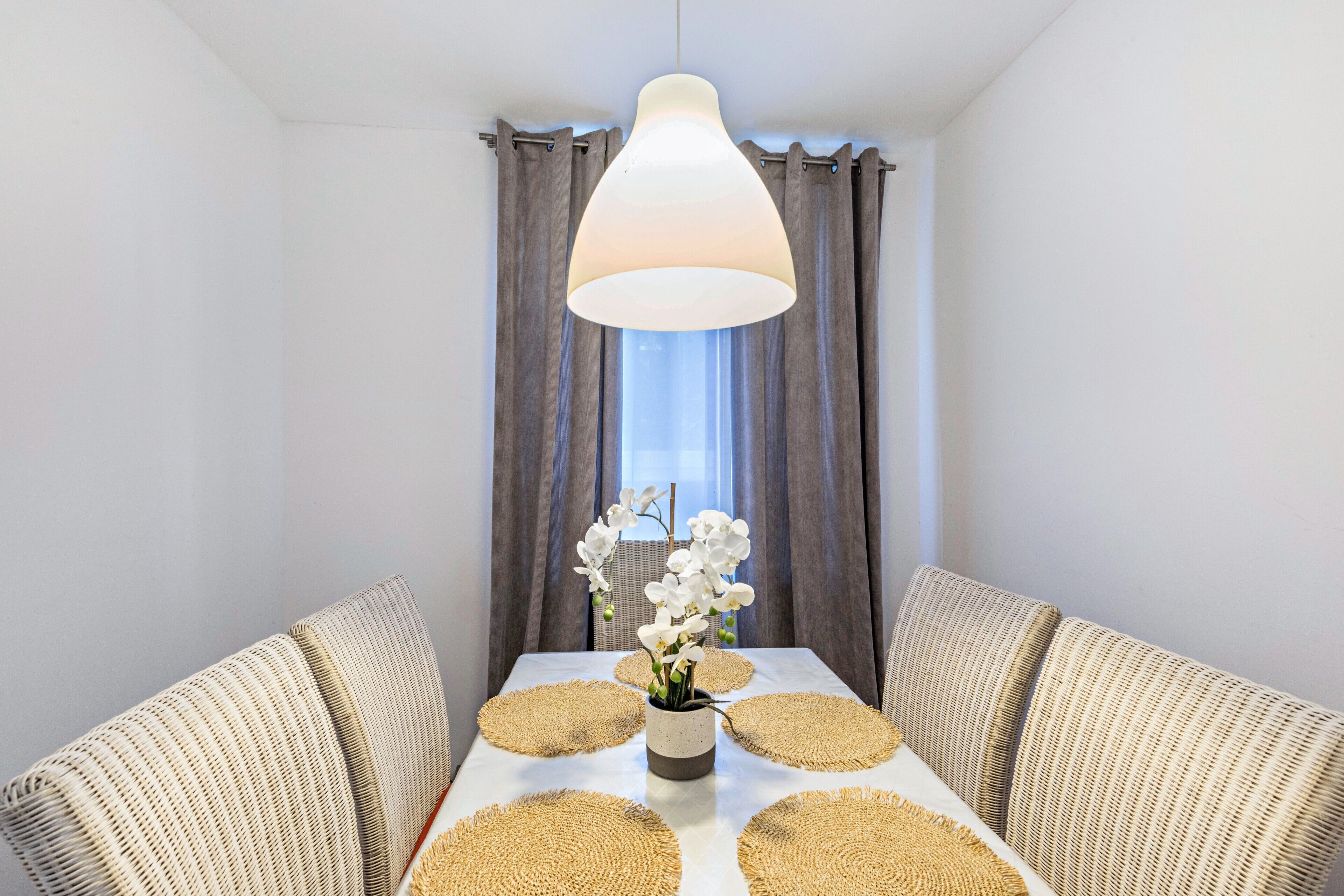Un espace repas comprenant une table, des chaises, un luminaire suspendu et une fenêtre avec des rideaux.