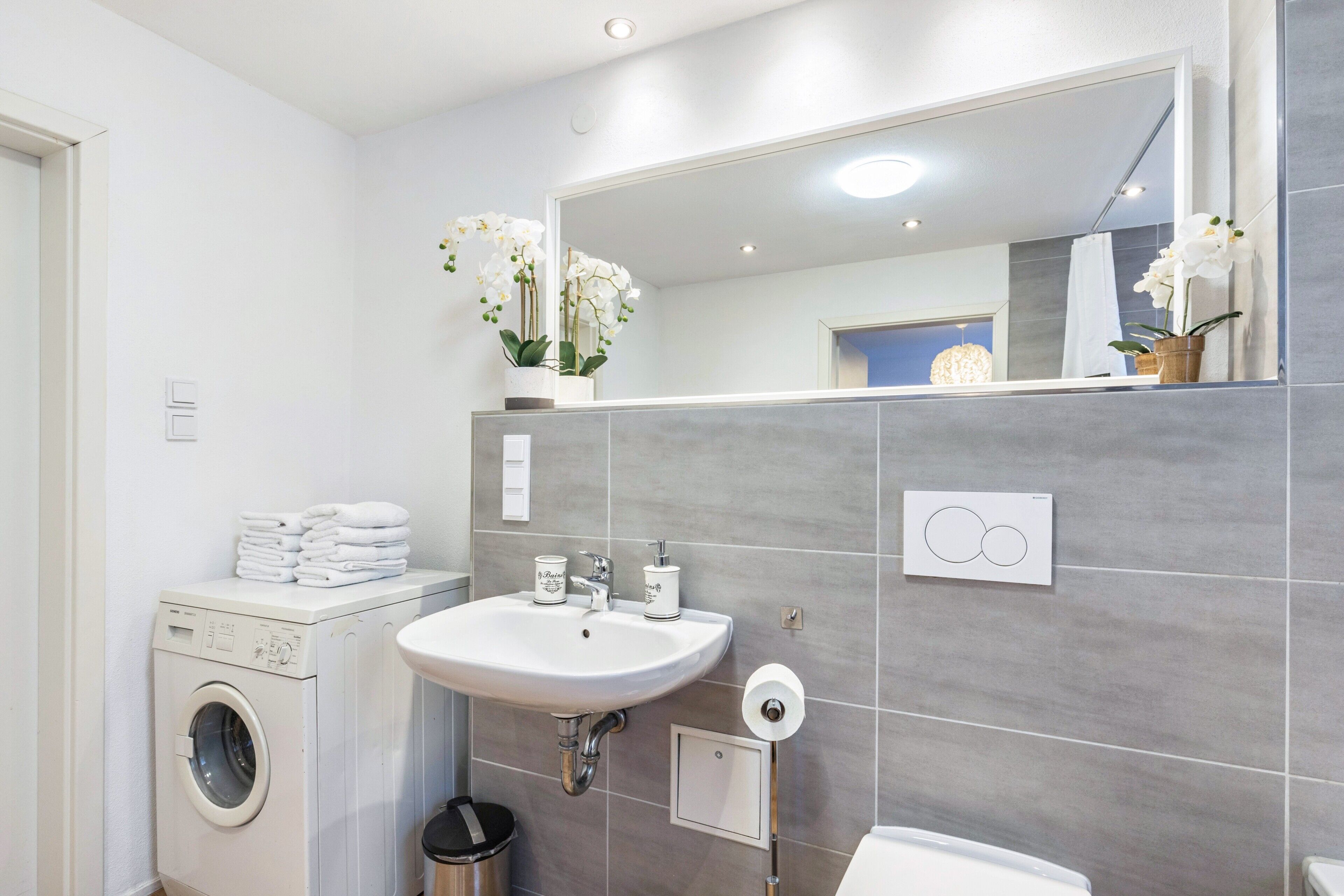 A modern bathroom with a washing machine, sink, mirror, and toilet.