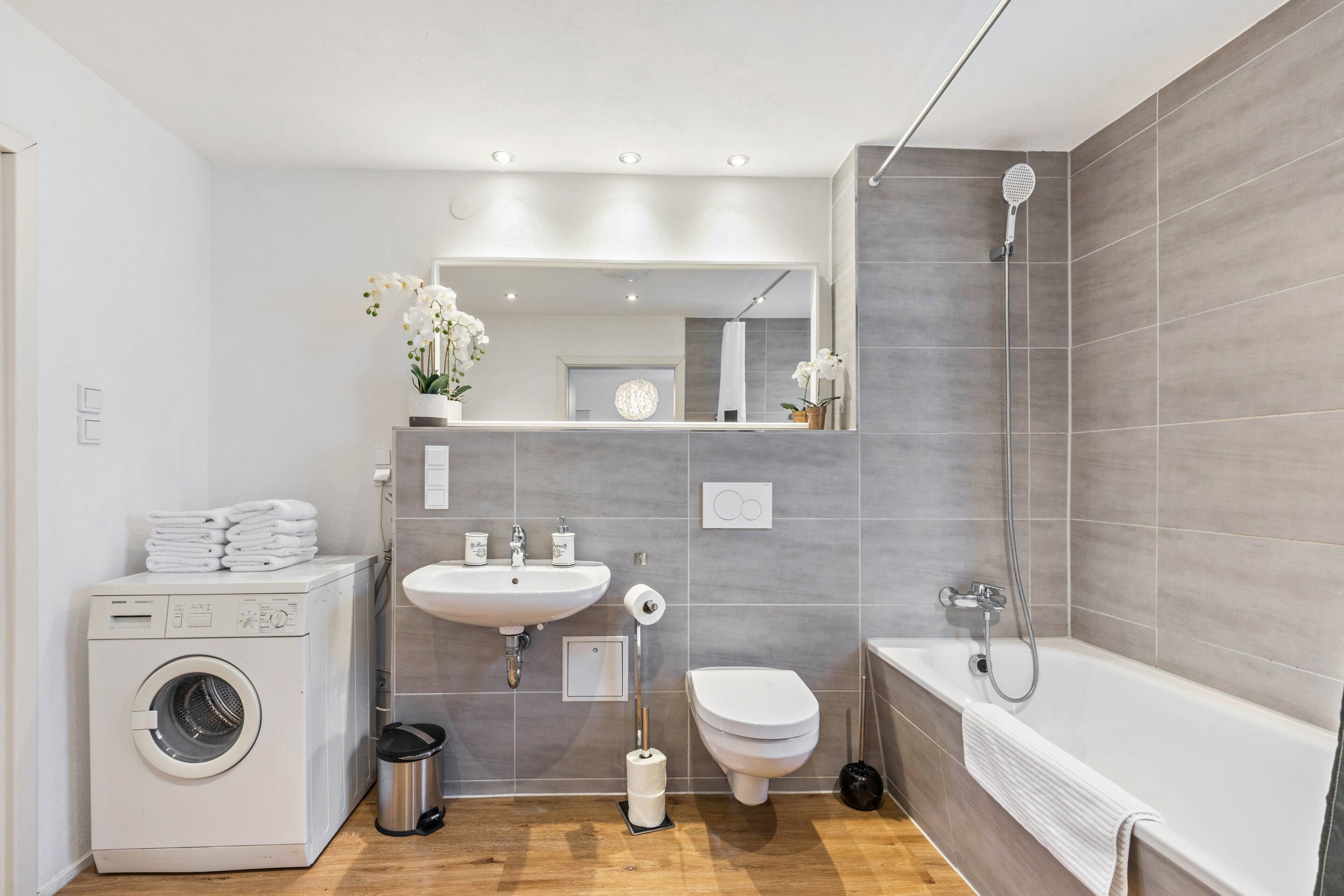 A modern bathroom with a washing machine, sink, toilet, and bathtub.