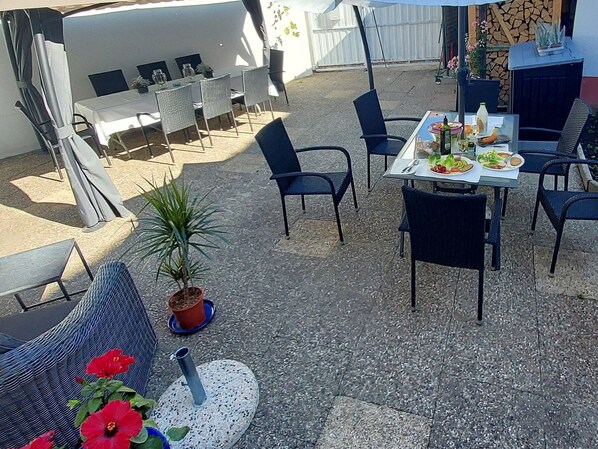 An outdoor patio with tables and chairs, a potted plant, and a small round table with a bottle and glasses.
