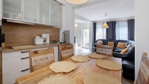 A modern kitchen with wooden cabinetry, a dining table with woven placemats, and a black leather sofa in the living area.