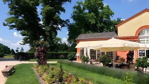 A cafe with outdoor seating, surrounded by a garden with various plants and flowers.
