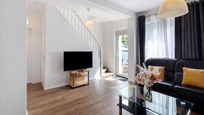 A modern living room with a staircase, a flat-screen TV, a glass coffee table, and a black leather sofa.