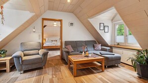 Une pièce de style « loft », avec un plafond en bois, un canapé, un fauteuil, une table basse et une fenêtre donnant sur un paysage agréable.