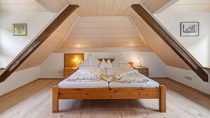 Une chambre avec un plafond en pente, un cadre de lit en bois, deux tables de chevet et un luminaire fixé au mur.