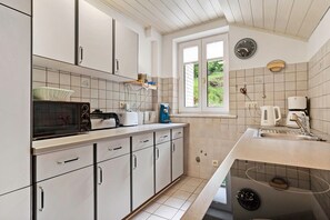 A kitchen with white cabinets, a microwave, a toaster, a coffee maker, and a window with a view of greenery. - Apartment 'Altes Forsthaus - Fewo Bianca' with Mountain View, Private Terrace and Wi-Fi (Bad Peterstal-Griesbach)