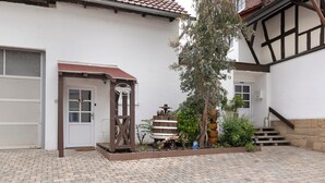 Un patio con un edificio blanco, un portón de madera, un banco y una planta en maceta.