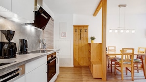 A modern kitchen with white cabinets, a built-in oven, a coffee maker, and a wooden dining area with a table and chairs. - Apartment 2 – Well-Equipped Kitchen & Spacious Outdoor Area with Beautiful Nature Views (Kirchseeon)