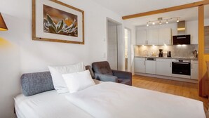 A bedroom with a bed, a chair, and a kitchenette in the background. - Apartment 2 – Well-Equipped Kitchen & Spacious Outdoor Area with Beautiful Nature Views (Kirchseeon)