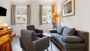 A living room with a sofa, armchair, TV, lamp, and a framed picture on the wall. - Apartment 2 – Well-Equipped Kitchen & Spacious Outdoor Area with Beautiful Nature Views (Kirchseeon)