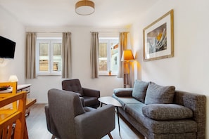 Ein Wohnzimmer mit Sofa, Sesseln, Fernseher, Lampe und einem gerahmten Bild an der Wand.