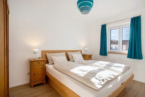 Makuuhuoneessa on puinen sänky, yöpöydät, ikkuna, jossa on verhot, ja kattovalaisin.