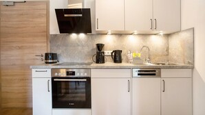 A modern kitchen with white cabinets, a built-in oven, a dishwasher, and a coffee maker. - Apartment 4 – Well-Equipped Kitchen, Spacious Outdoor Area, and Beautiful Nature Views (Kirchseeon)