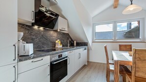 A modern kitchen with white cabinetry, a black oven, a marble countertop, and a dining area with wooden chairs. - Apartment 10 – Two-Level Living with Separate Bedroom and Well-Equipped Kitchen (Kirchseeon)