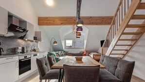 Une cuisine moderne dotée d’appareils électroménagers intégrés, un coin repas avec une table et des chaises en bois, et une chambre en mezzanine accessible par un escalier en bois.