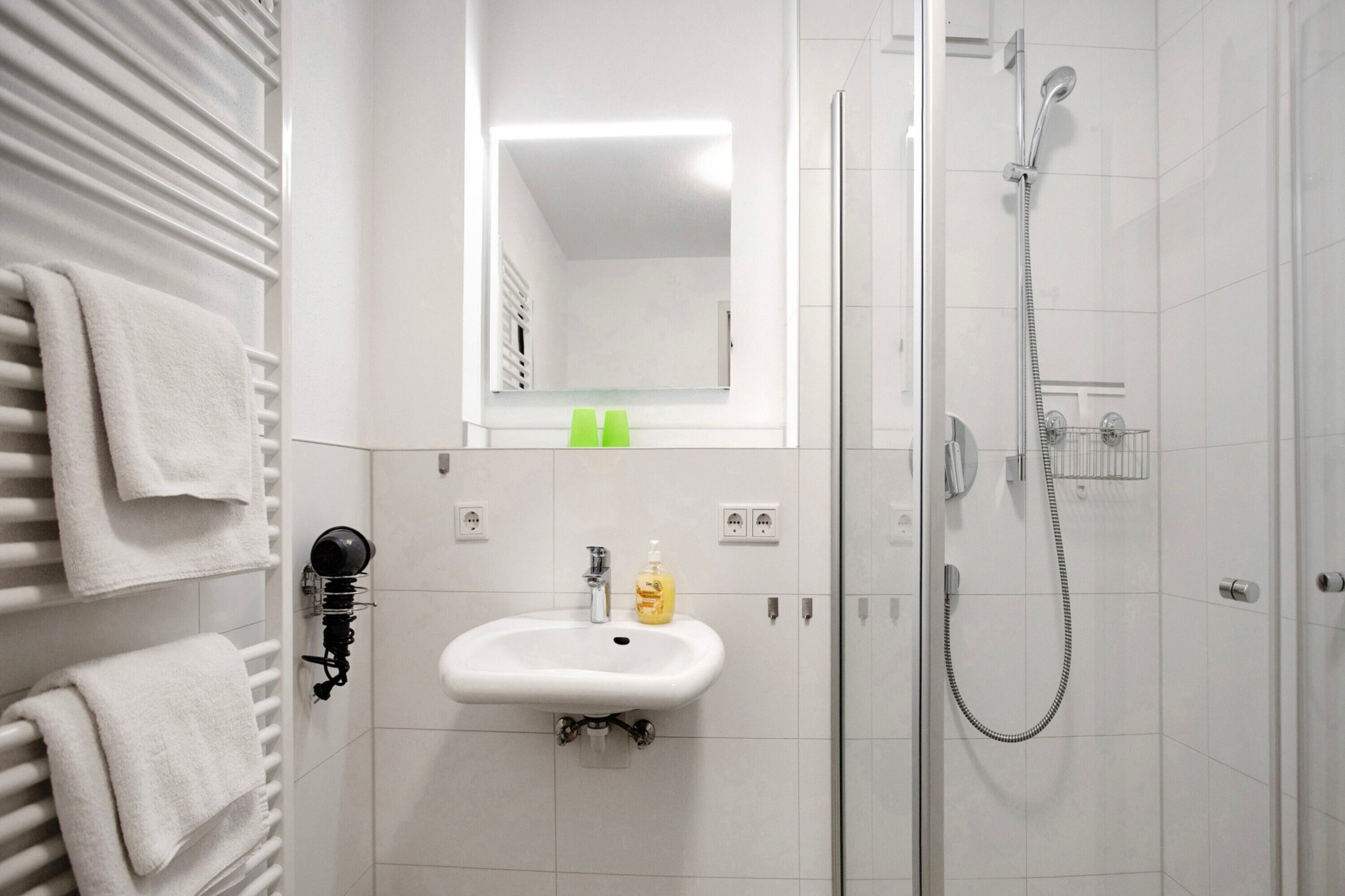 Ein Badezimmer mit einem weißen Waschbecken, einem Spiegel, einer Dusche und Handtuchhaltern.