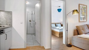 A modern apartment with a kitchen, a shower room, a bed with a wooden headboard, and a floor lamp. - Apartment 1 – Well-Equipped Kitchen, Spacious Outdoor Area, and Lovely Nature Views (Kirchseeon)