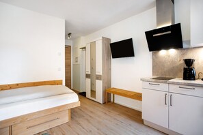 A bedroom with a bed, a bench, a white wardrobe, a TV, and a coffee maker. - Studio Apartment 'Appartement 7' with Shared Terrace, Shared Garden and Wi-Fi (Kirchseeon)