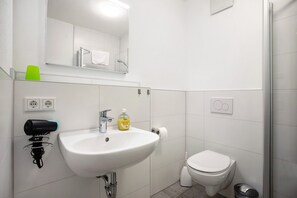 Ett modernt badrum med ett vitt handfat, en toalett och en dusch.
