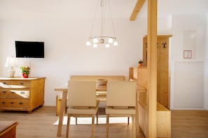 Un coin repas avec une table et des chaises en bois, un lustre, un téléviseur et un meuble en bois orné d’une plante.