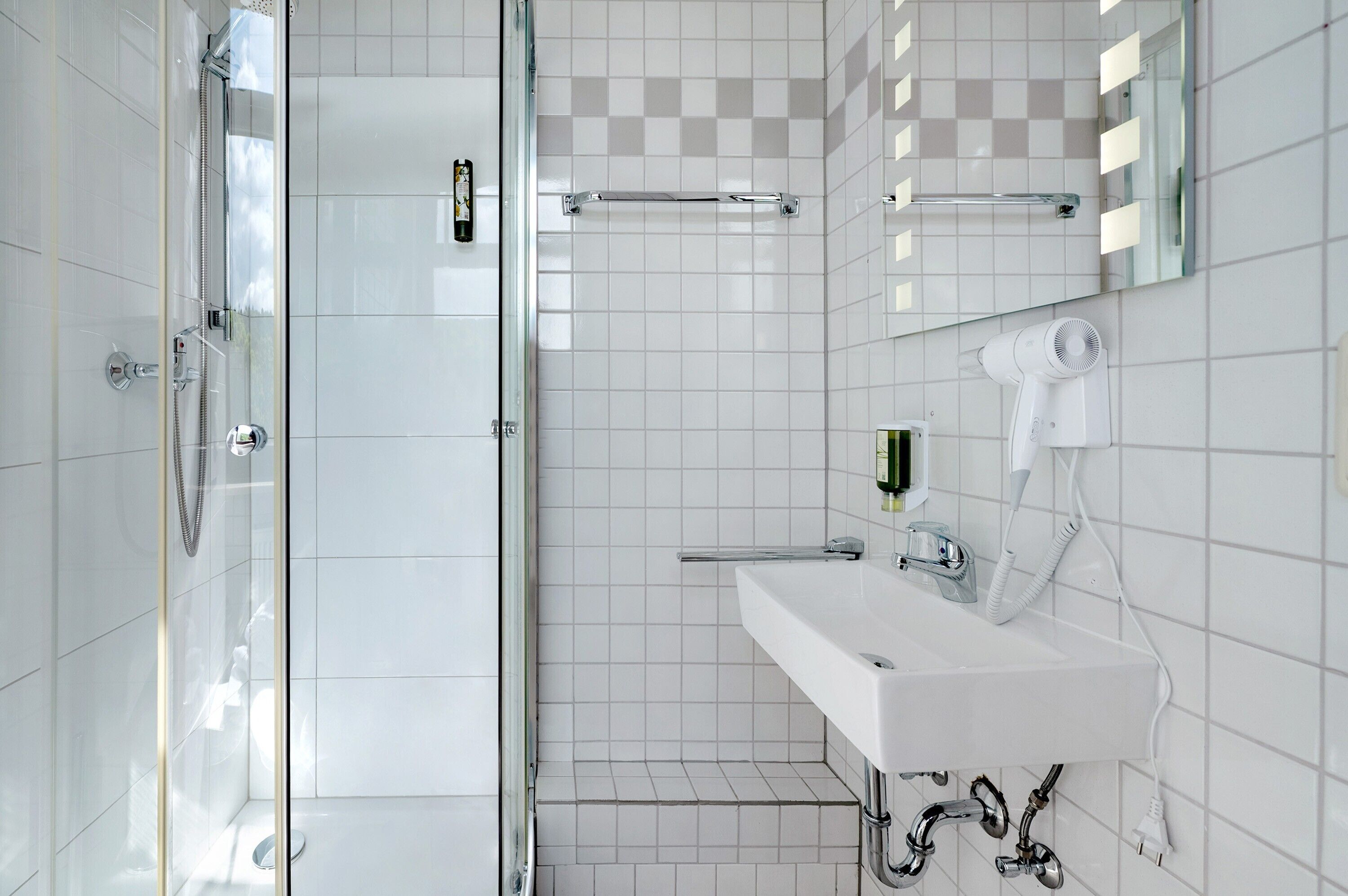 Une salle de bain moderne avec une douche à parois de verre, un lavabo blanc avec un miroir et un sèche-cheveux fixé au mur.