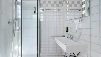 Une salle de bain moderne avec une douche à parois de verre, un lavabo blanc avec un miroir et un sèche-cheveux fixé au mur.