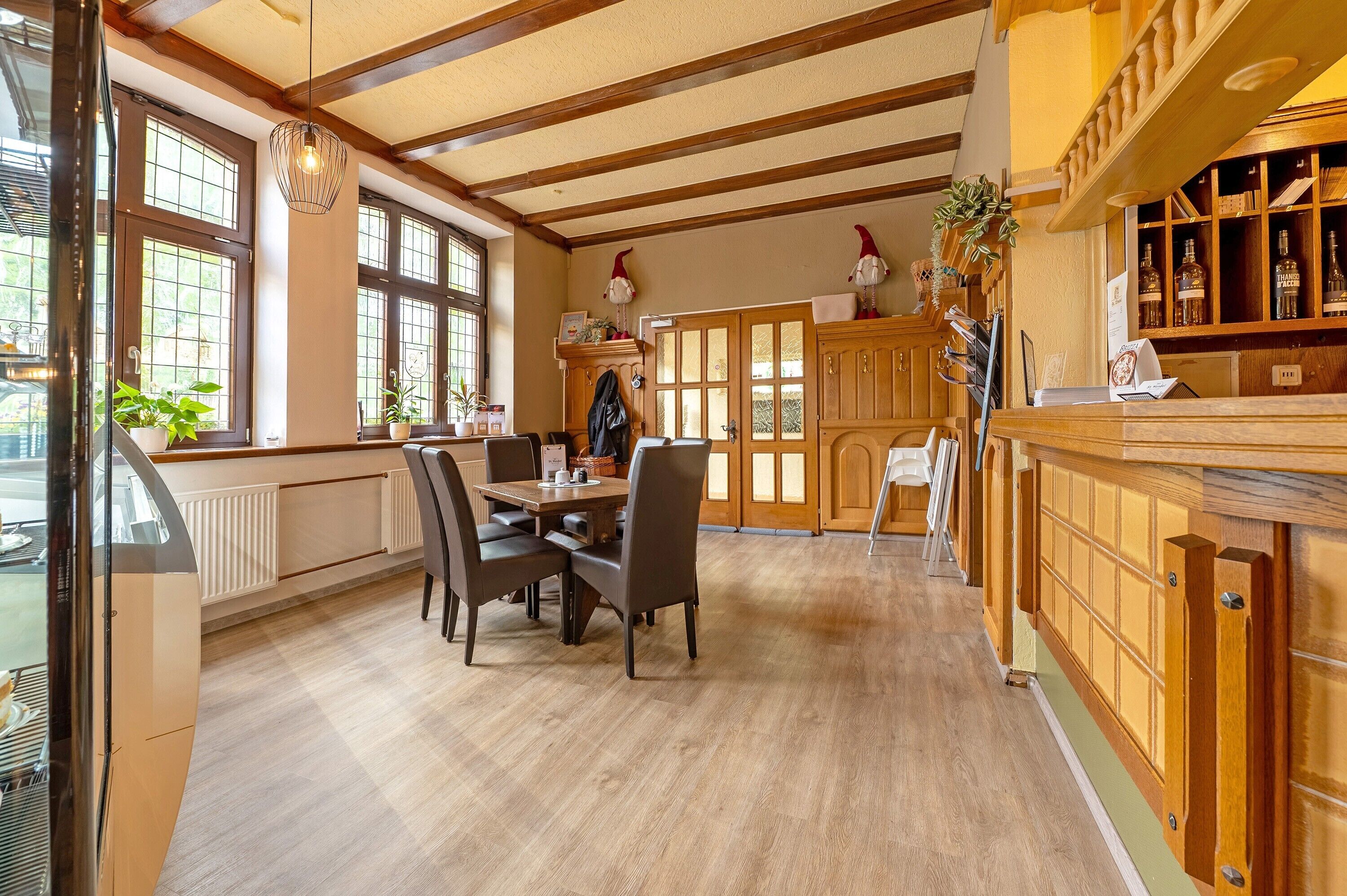 Un coin repas avec une table et des chaises en bois, un comptoir de cuisine avec une étagère remplie de bouteilles, et de grandes fenêtres offrant une vue dégagée.