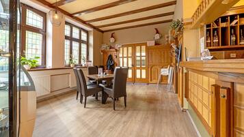 Un coin repas avec une table et des chaises en bois, un comptoir de cuisine avec une étagère remplie de bouteilles, et de grandes fenêtres offrant une vue dégagée.